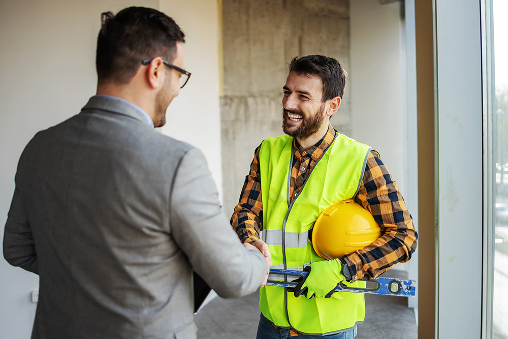 Smiling construction worker shaking hands with supervisor while standing in building in construction process.